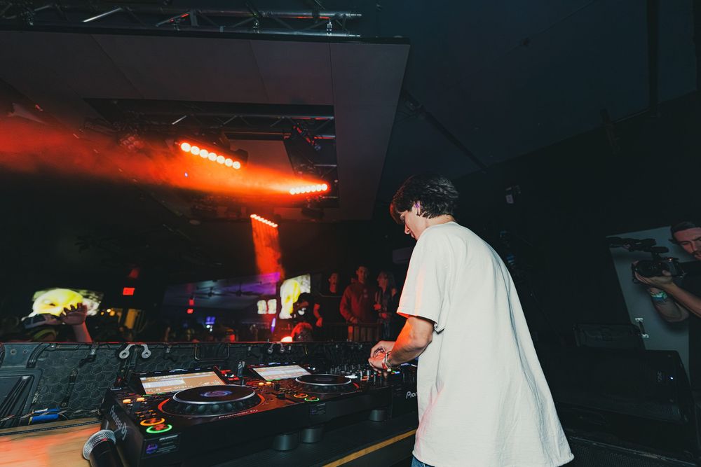 DJ performs at a dark nightclub with turntables and mixing equipment under moody lighting.