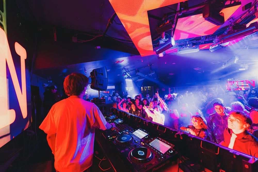 DJ performing at a nightclub with vibrant red and blue lighting creating an energetic atmosphere.