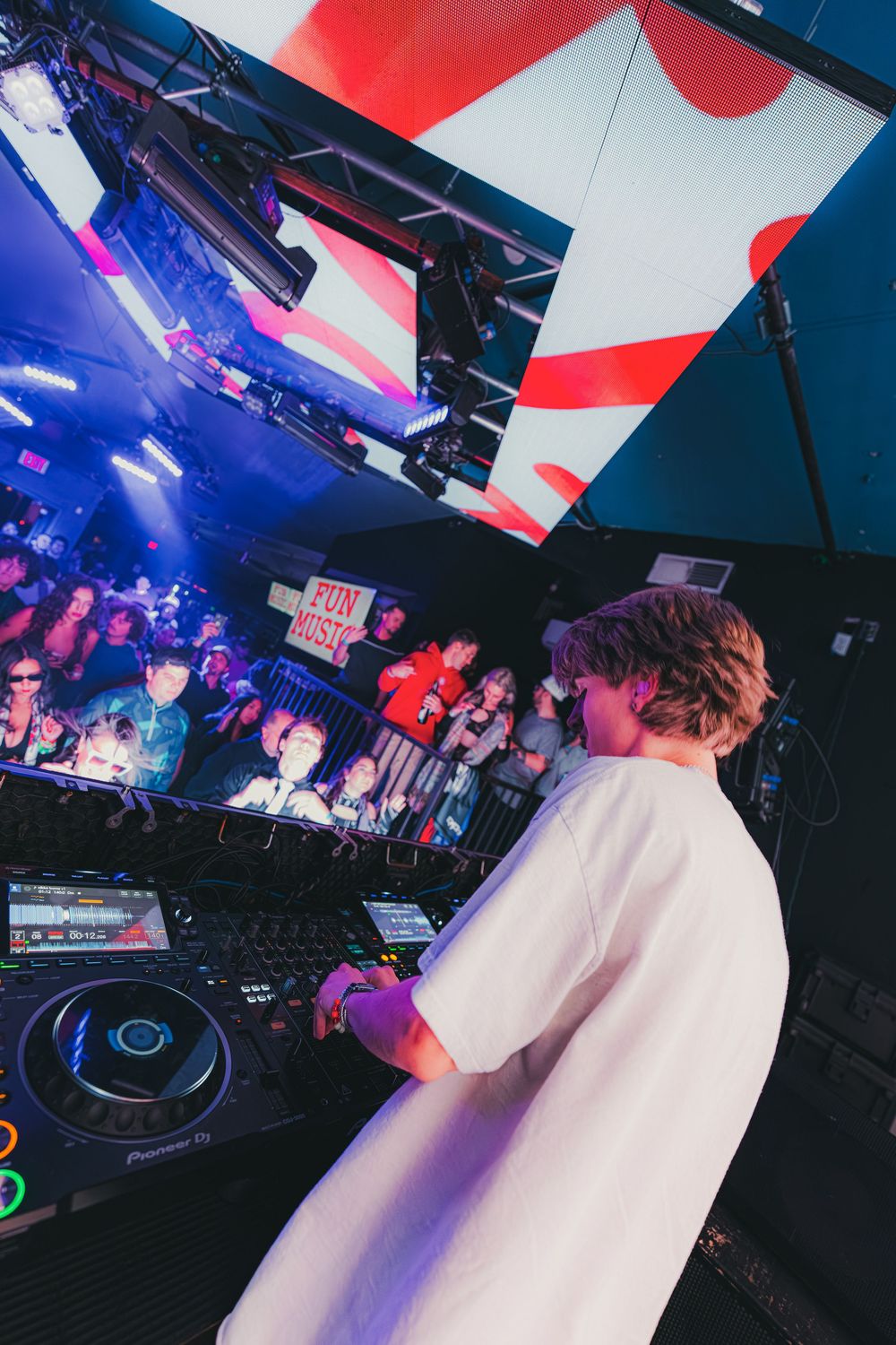 DJ performs at nightclub with colorful lighting and large screens displaying visuals in background.