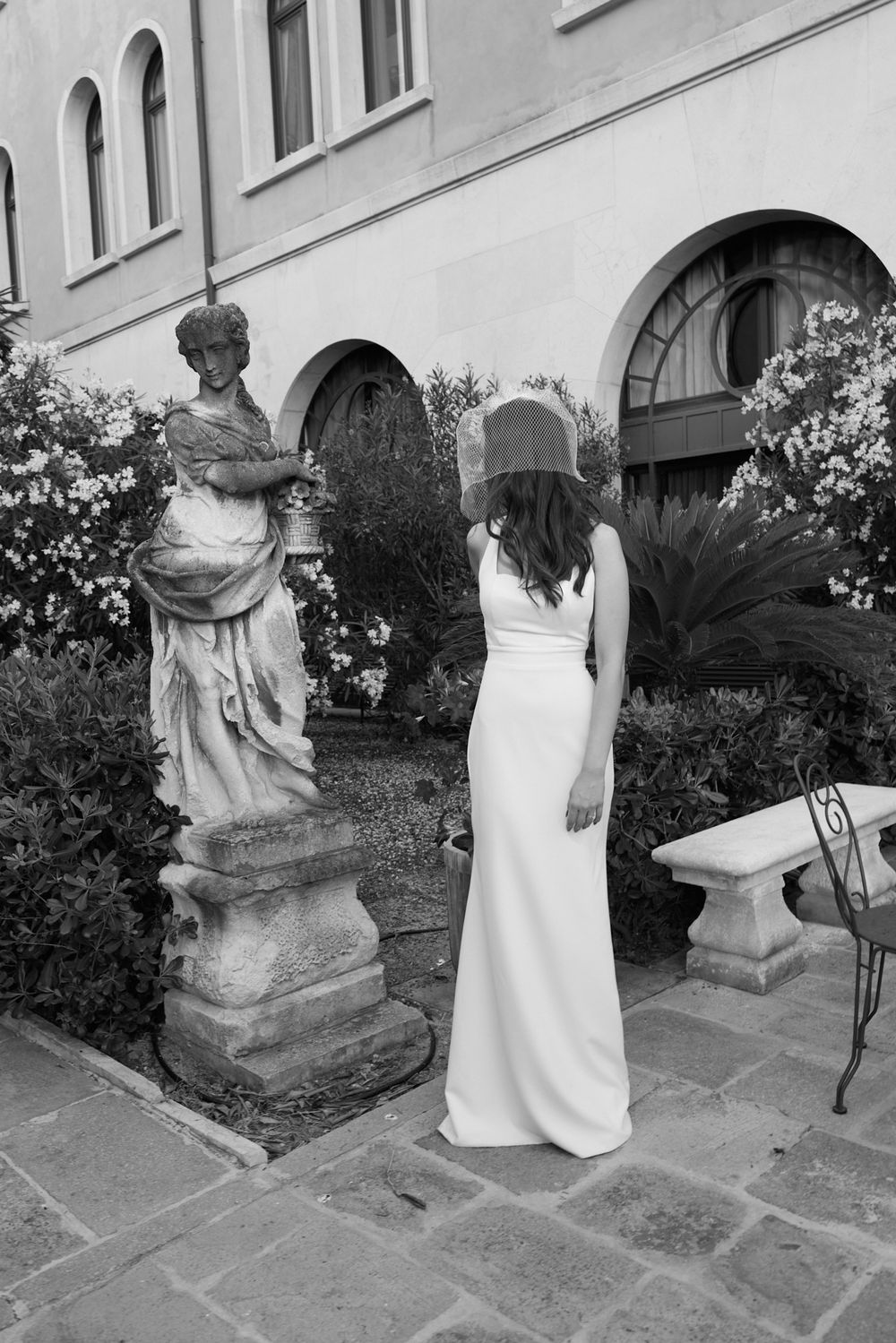 A woman in a white dress poses next to stone statues in a garden setting.