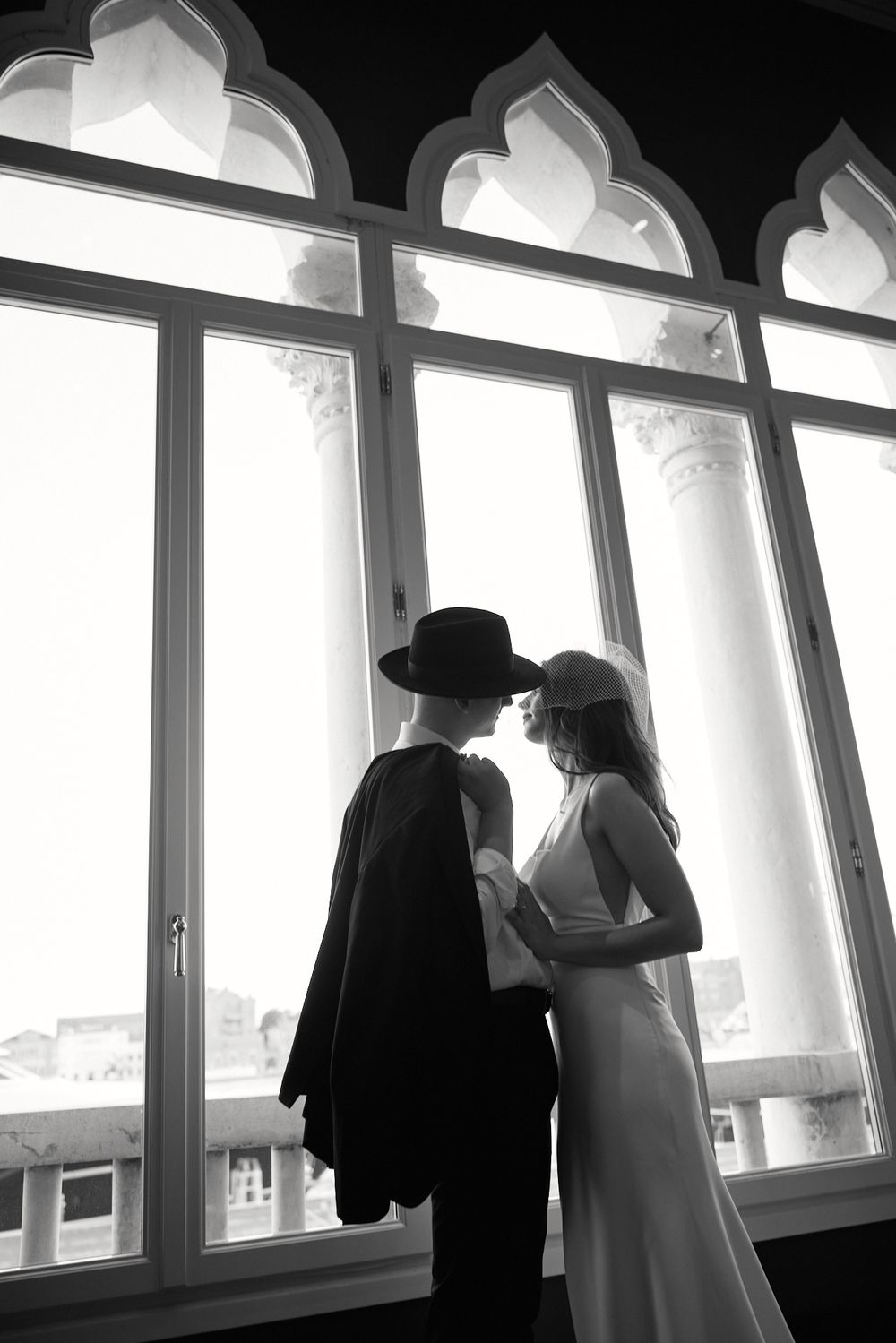 Silhouetted figures stand at large arched windows in a bright interior viewing area.