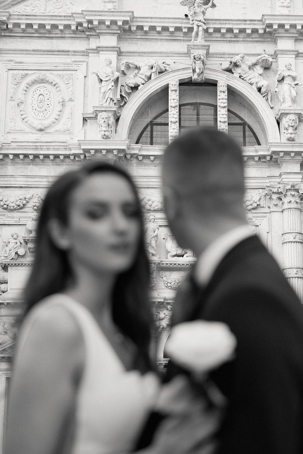 A romantic black and white wedding photo featuring an ornate architectural backdrop with decorative stonework.