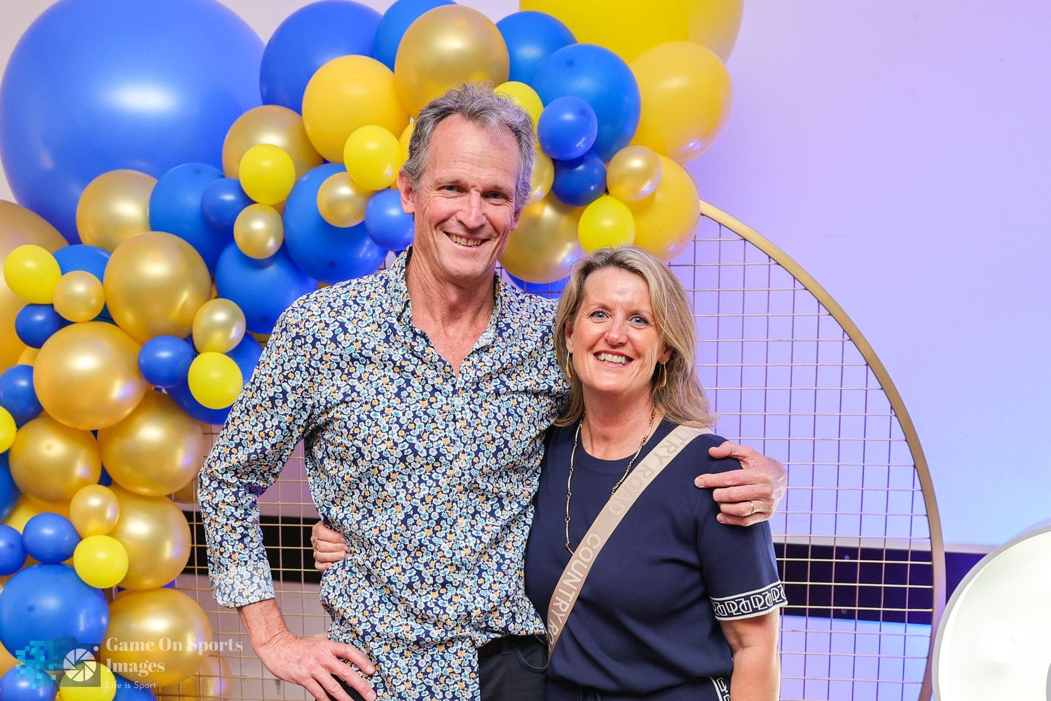 Couple celebrates with blue and gold balloon decorations at a festive party event.