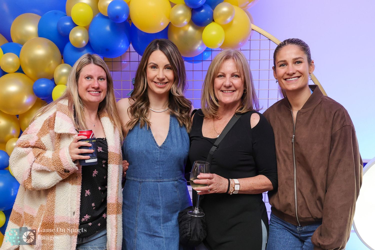 A group of people celebrating at a party with blue and gold balloon decorations in the background.