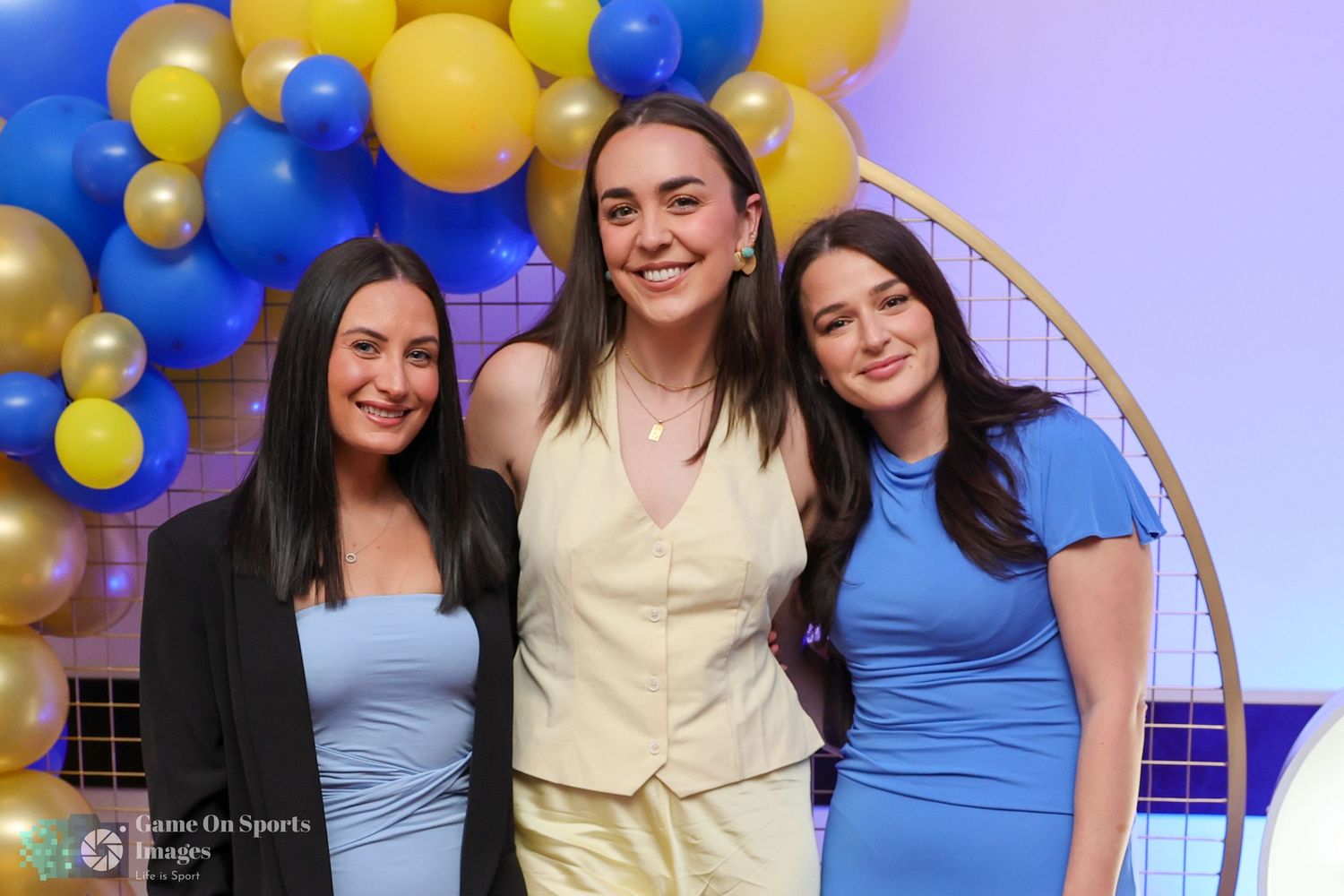 Celebratory event with blue, yellow and gold balloon arch decorations against a purple wall.