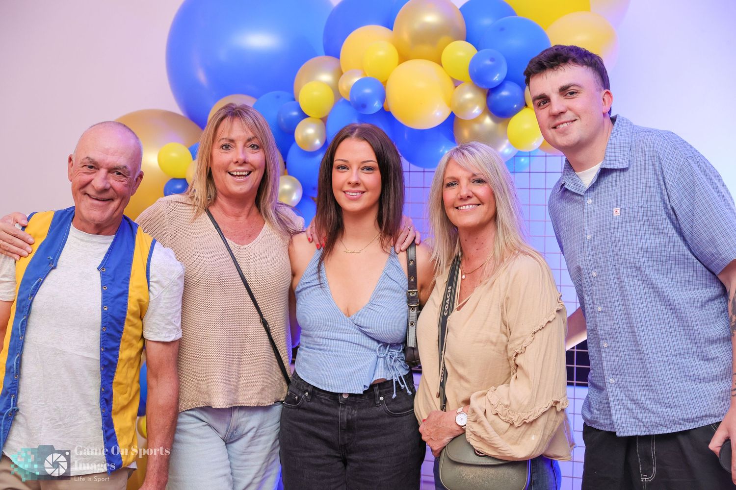 Group of people celebrating at a party with blue and yellow balloons in the background.