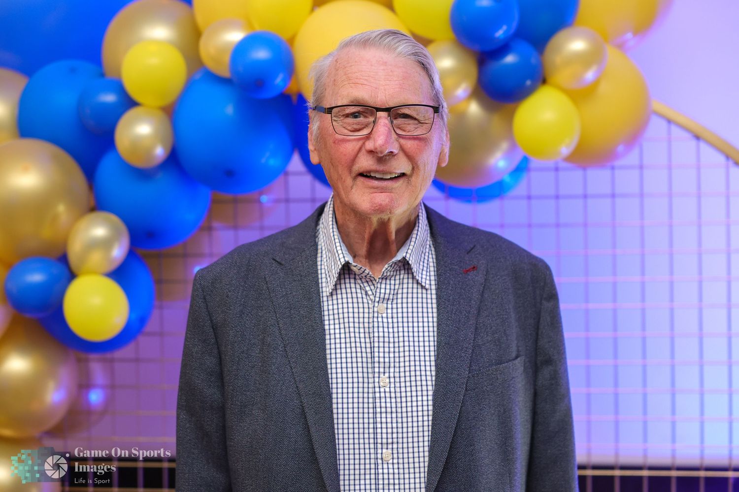 Festive celebration backdrop with blue, yellow and gold balloons decorating an indoor event space.