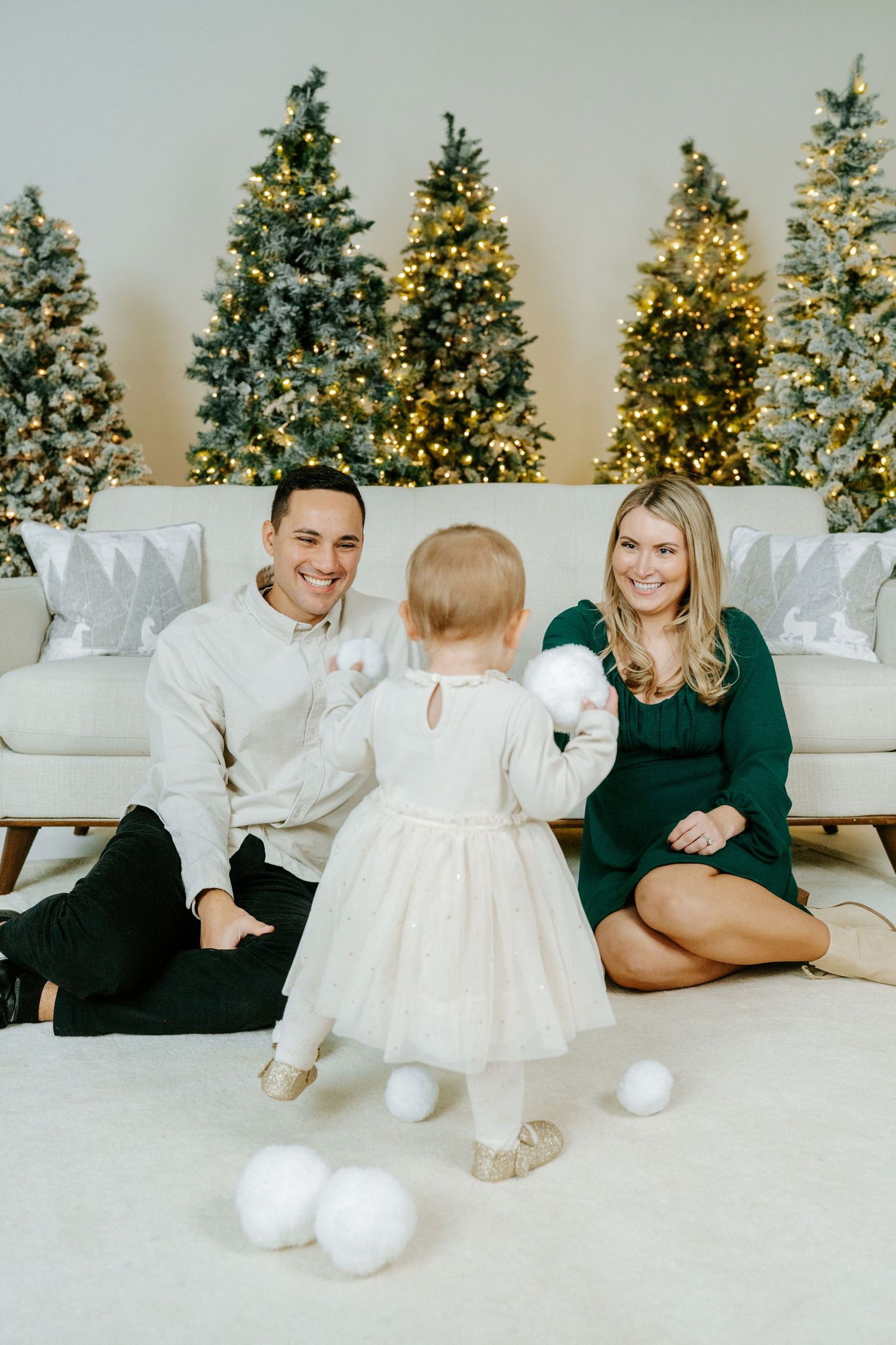 A holiday scene with decorated Christmas trees glowing in the background and white snowballs scattered on a light carpet.