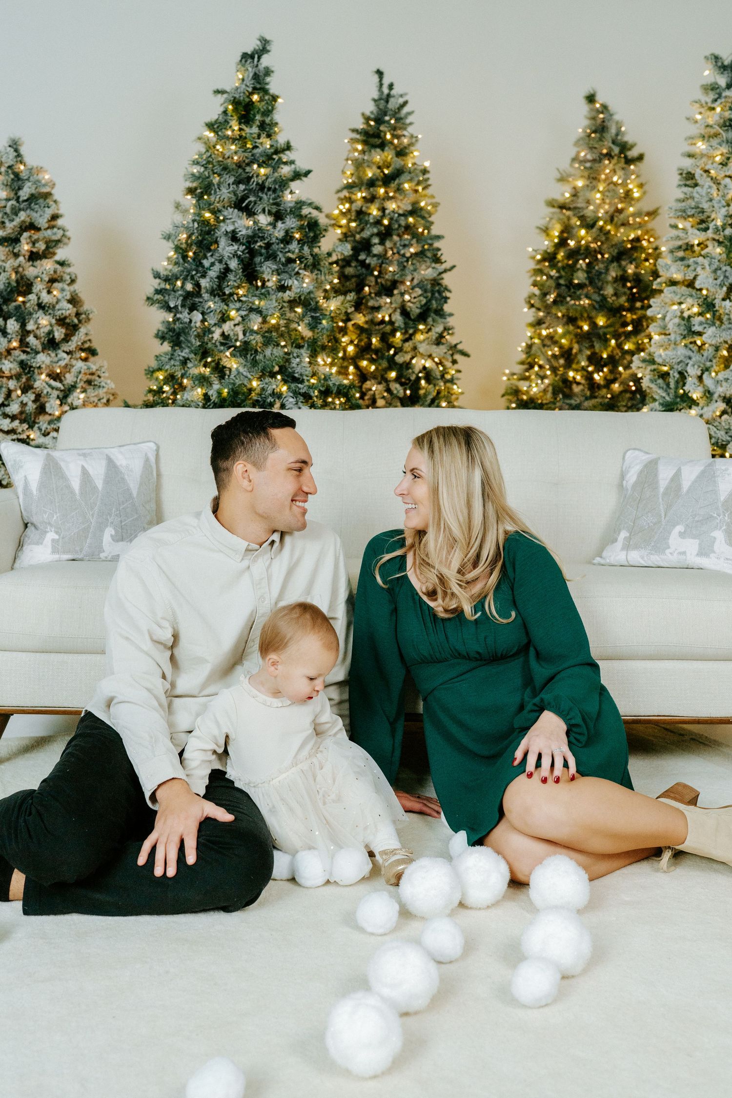 Family sitting on floor near decorated Christmas trees with white ornaments and silver decorations.