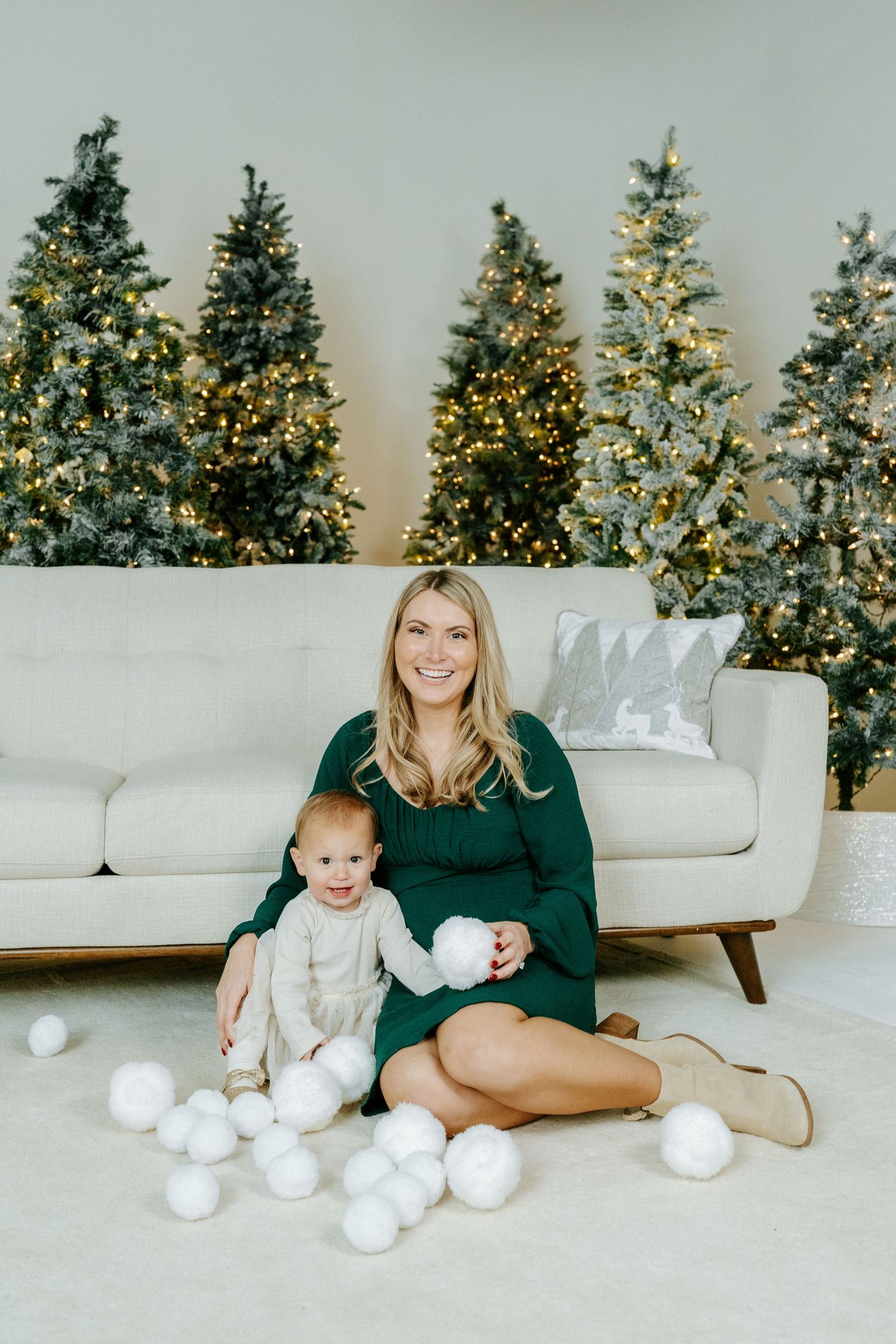 A family sits on a white couch with decorative snowballs scattered on the floor near illuminated Christmas trees.