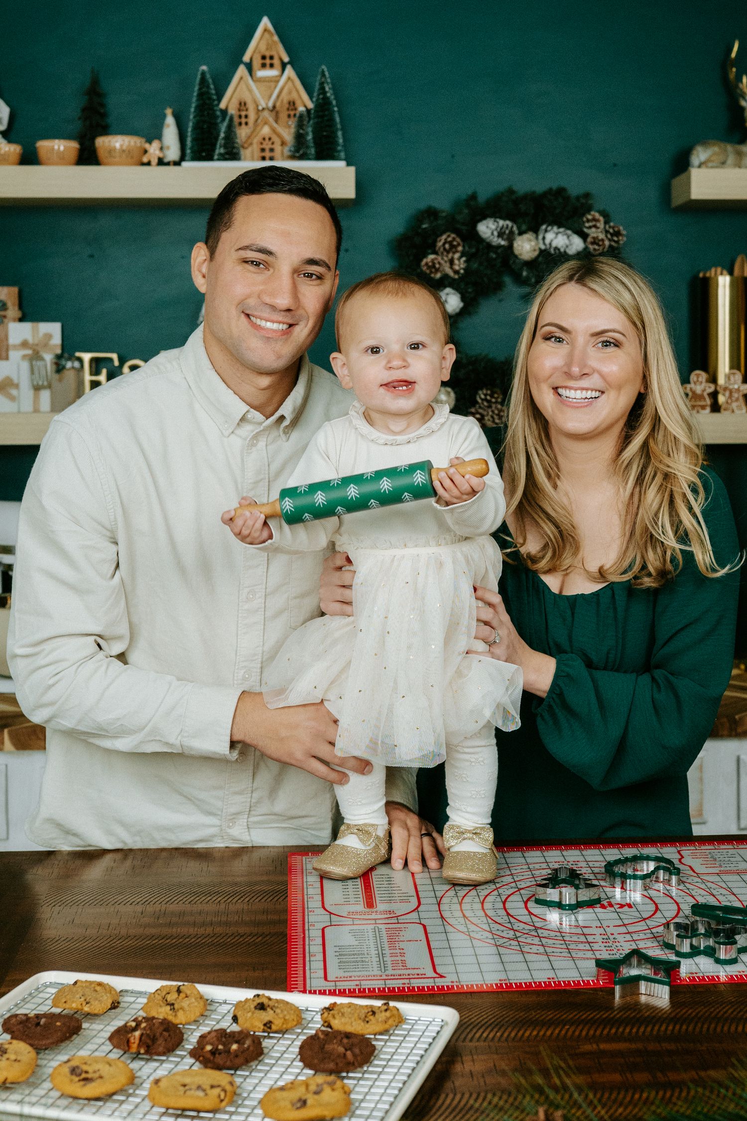Three people sit at a bakery counter with cookies and baked goods displayed on a cooling rack.