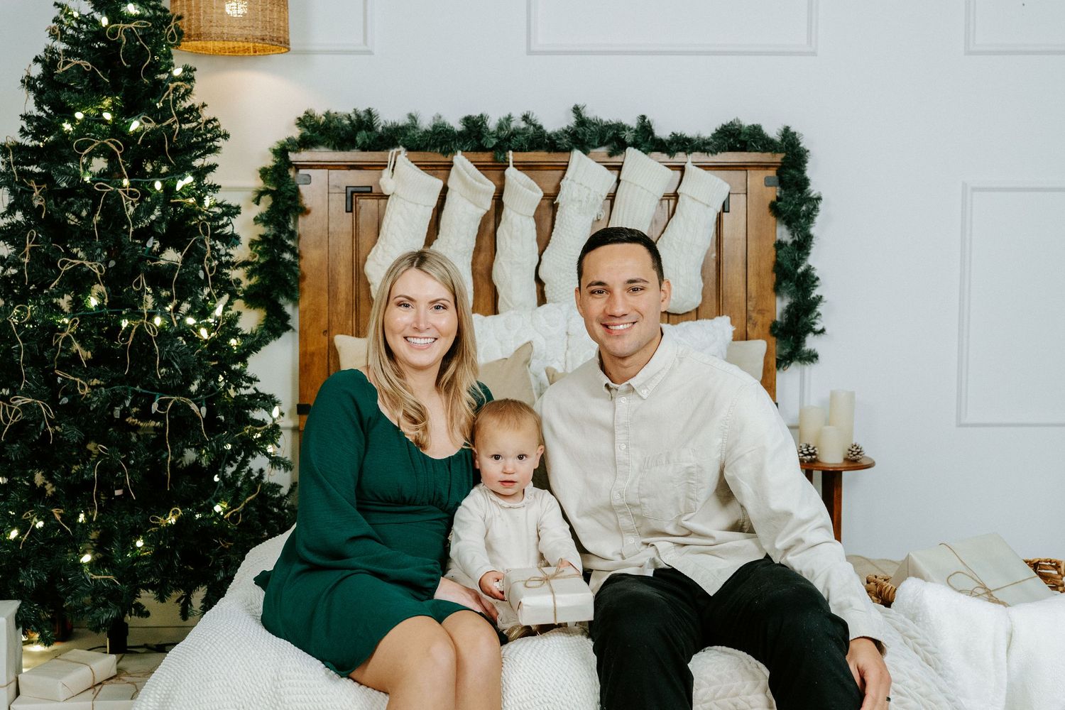 A family wearing coordinated green and white outfits poses for holiday photos in front of a Christmas tree.