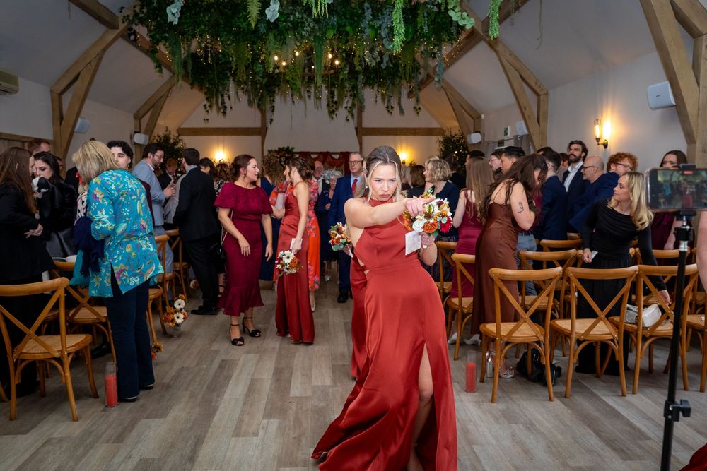 Bridesmaid in red dress dances joyfully inside a beautifully decorated barn wedding reception venue.