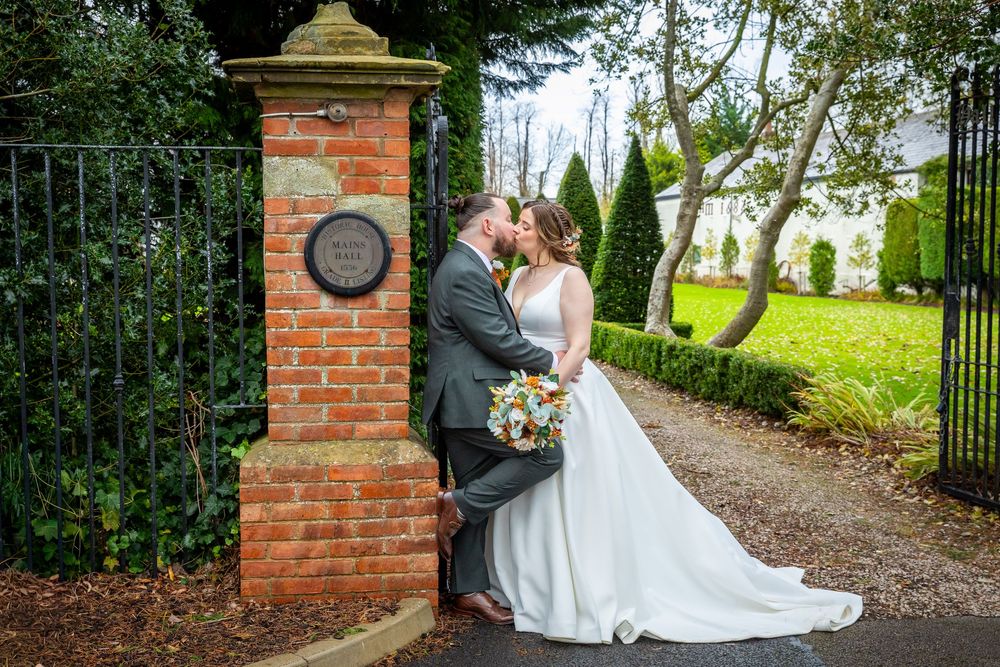 Bride and groom sharing a romantic moment by a brick gate pillar on their wedding day.