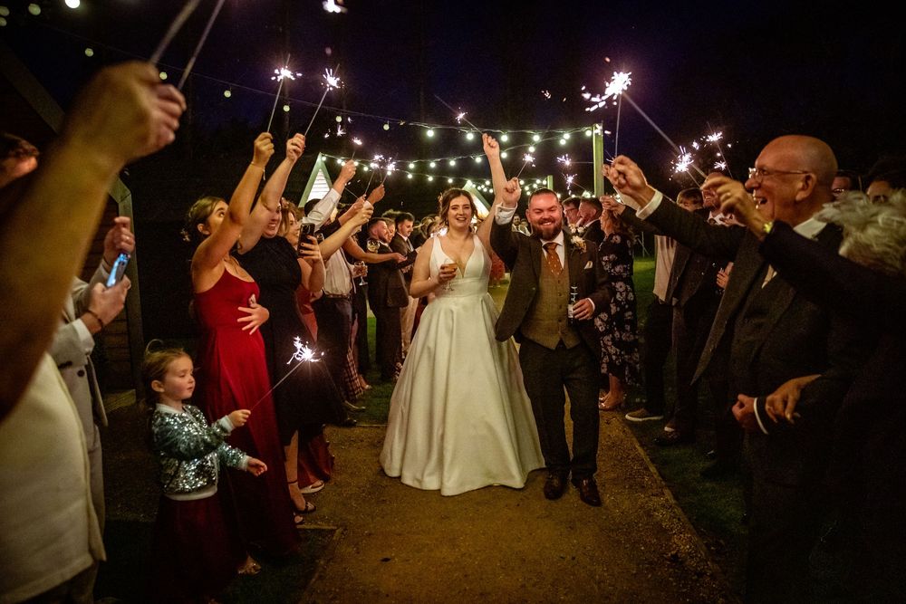 Bride and groom walking through a tunnel of sparklers held by cheering wedding guests at night.
