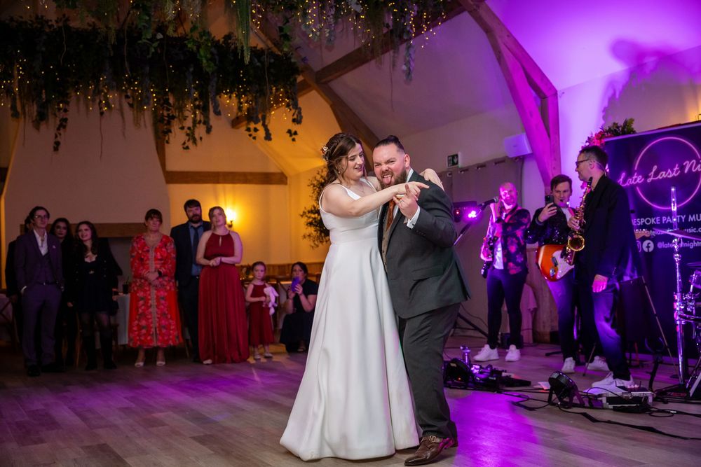 Bride and groom sharing their first dance on a wooden dance floor with a live band performing behind them.