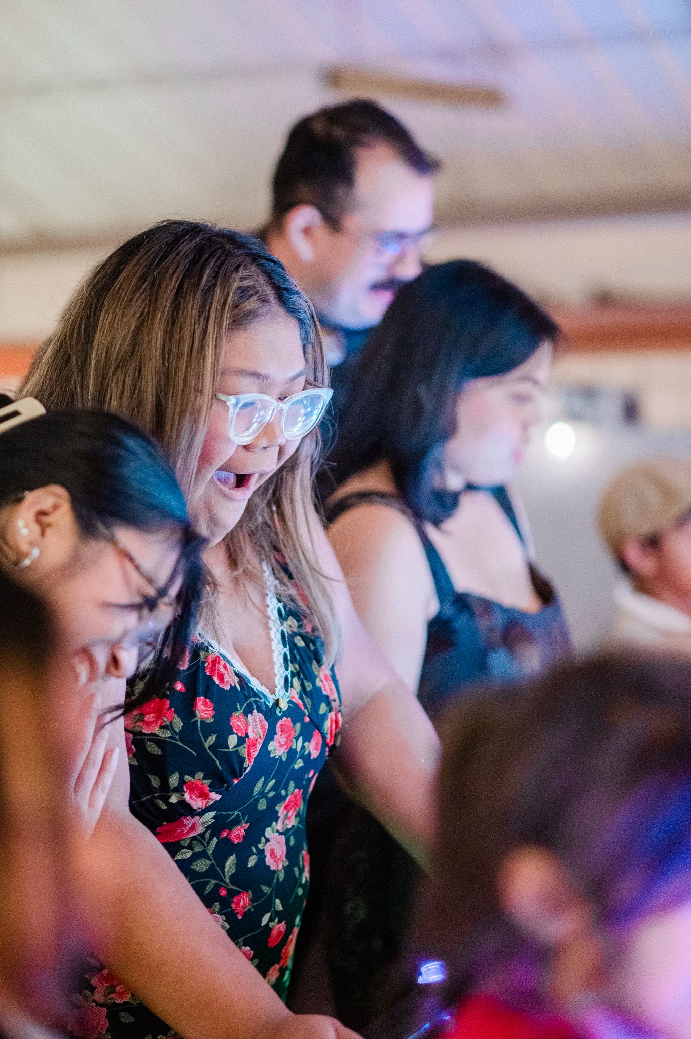 A group of people laugh and smile together at an indoor event with colorful lighting.