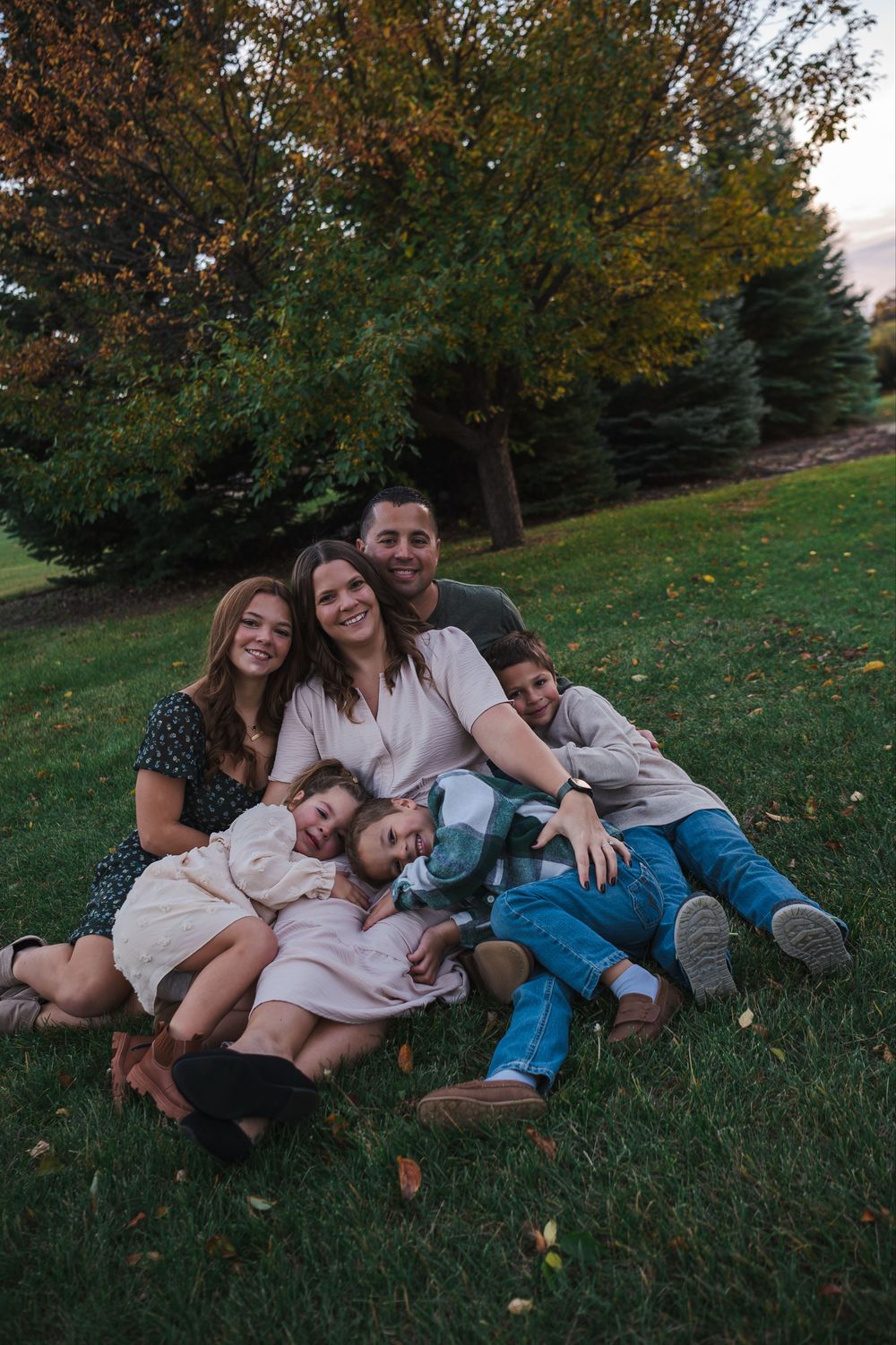 A group lounges together on green grass during a warm autumn day with trees in the background.