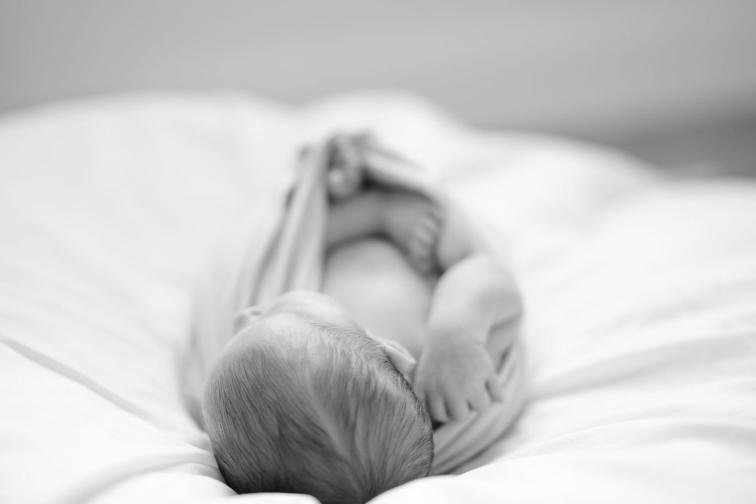 Black and white photo of a sleeping newborn baby lying on white sheets, showing tiny feet and head.