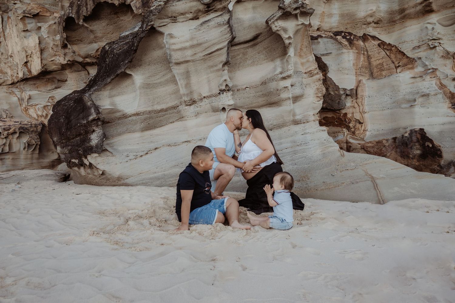Family sitting for a central coast maternity photo session infront of a rocky beach cave with natural stone formations.