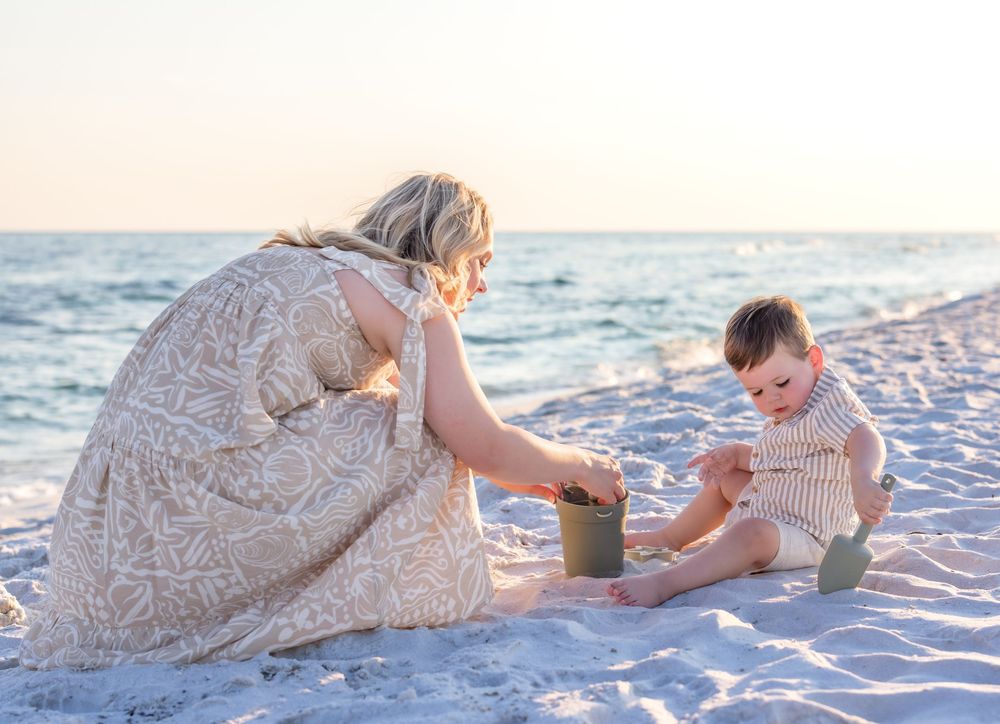 Mother and baby playing together on a sandy beach during golden hour.