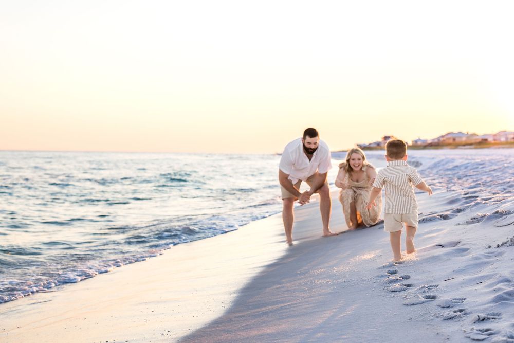 People walking along the shoreline of a beach during golden hour with gentle waves rolling in.