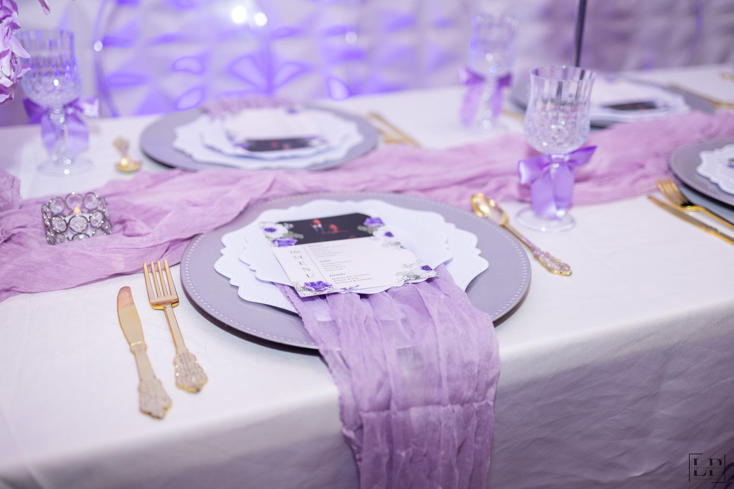 An elegant table setting with purple accents, white plates, and gold cutlery.