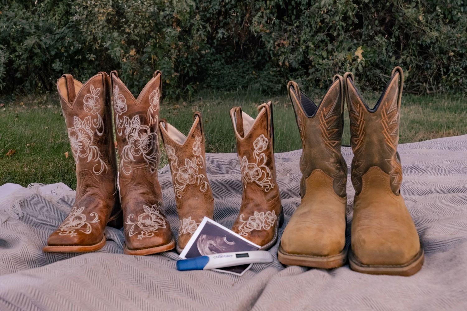 A collection of brown leather cowboy boots arranged in a row on a porch or walkway.