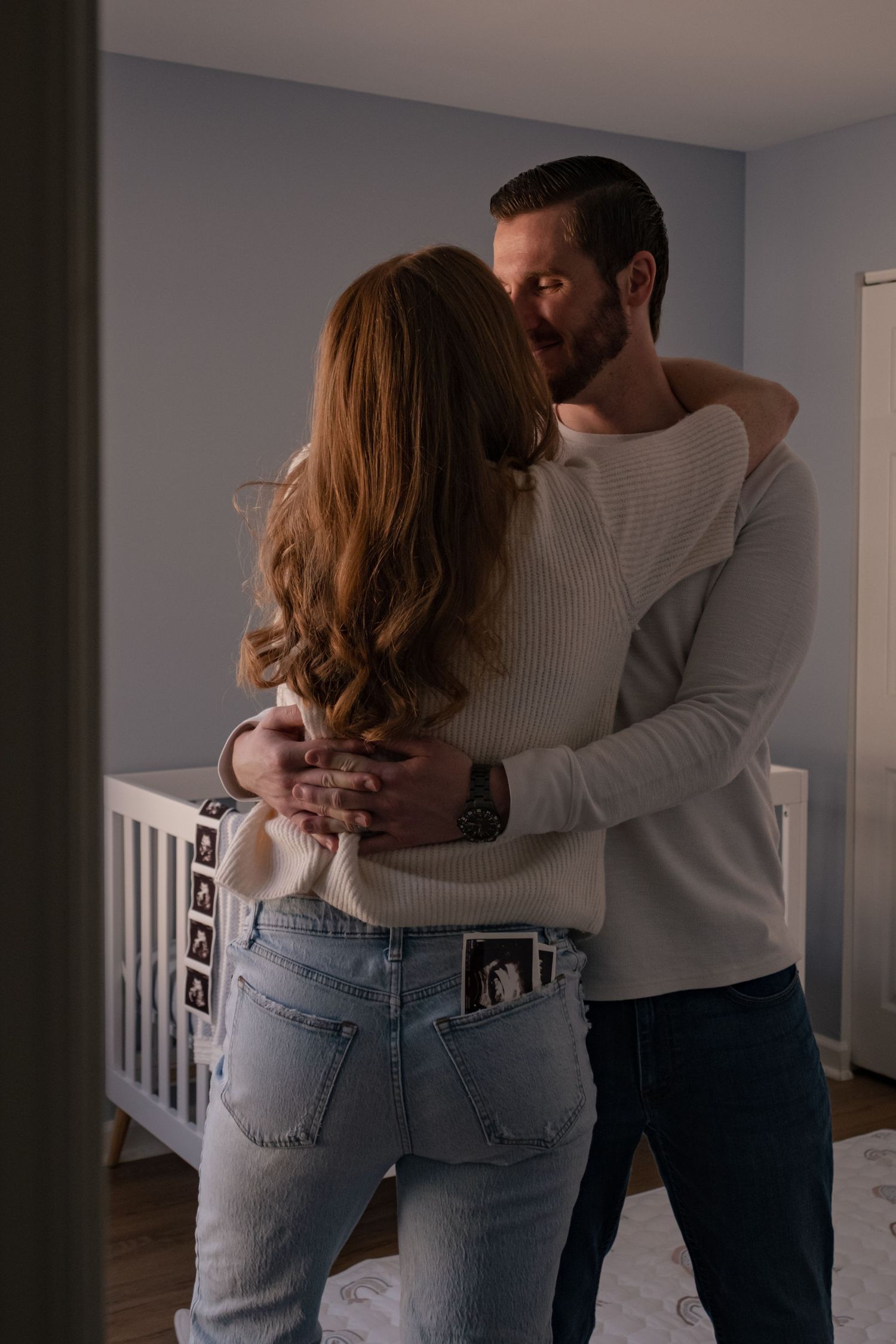 A couple in casual attire embraces in a dimly lit room with gray walls, shown in a series of intimate poses.