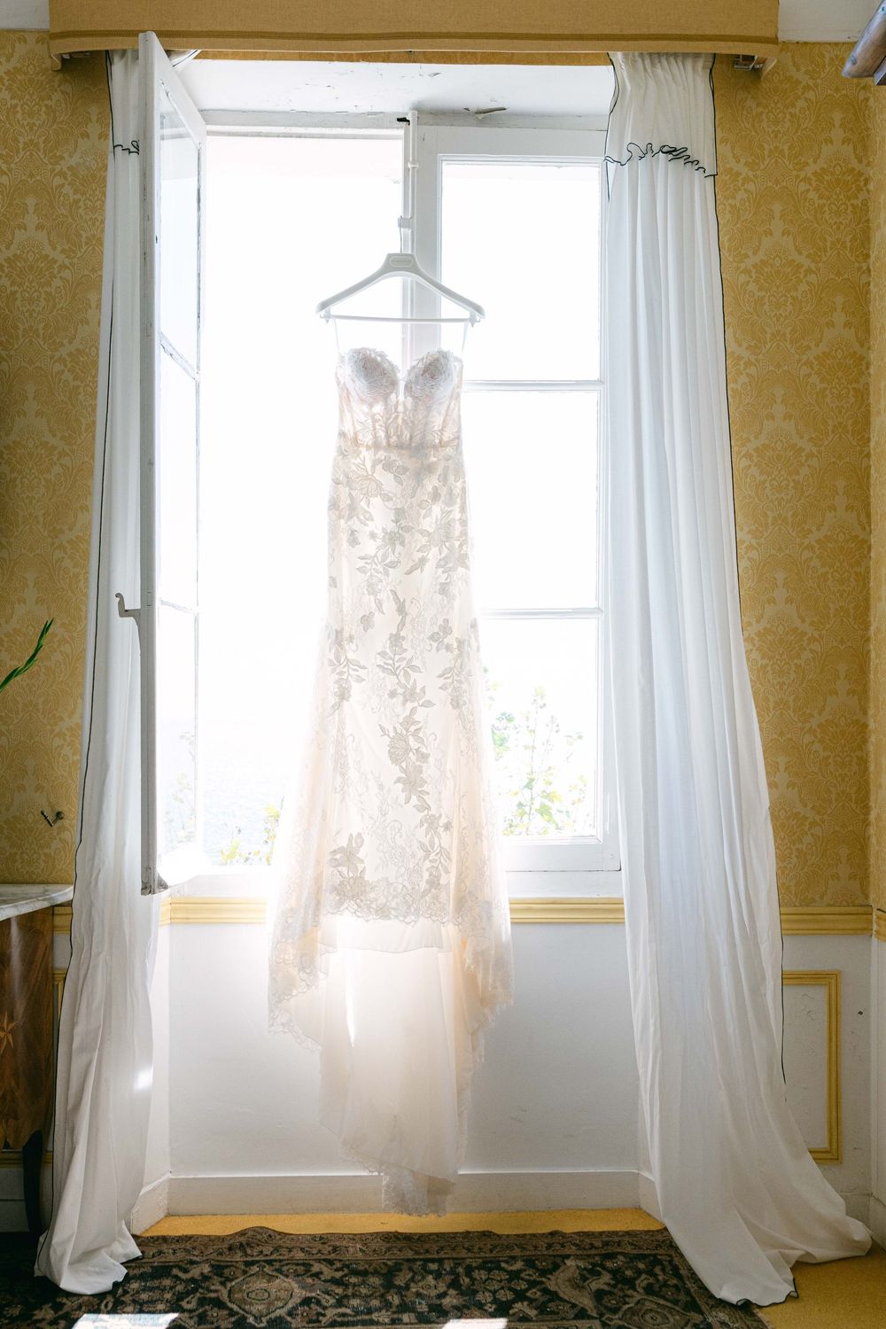 Three white sheer curtains hanging in front of bright windows in a room with yellow walls and wainscoting.