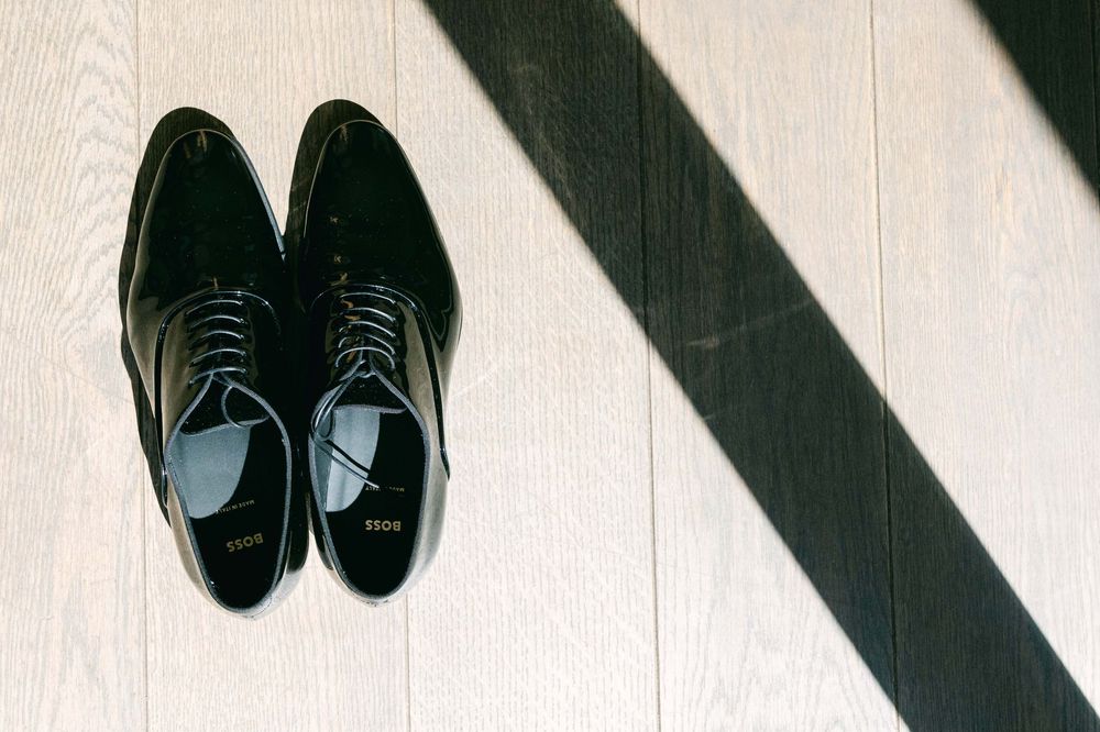 A row of black dress shoes and boots arranged in a line on a light wooden floor.