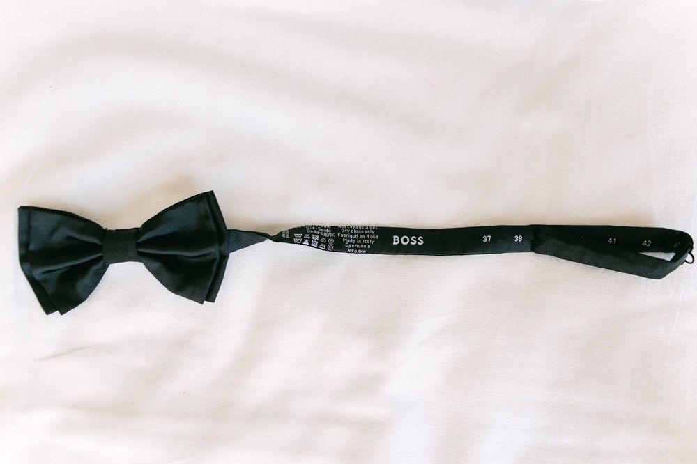 A black bow tie displayed on a white surface next to its reflection.