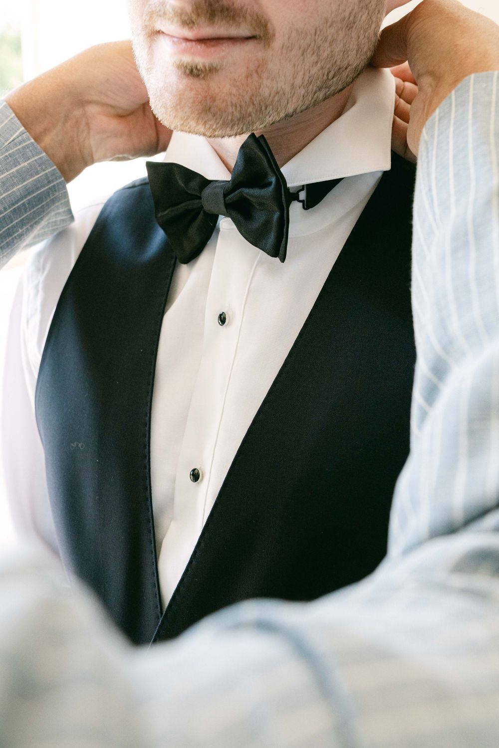 Close-up view of formal black bow tie and white dress shirt with black vest in classic tuxedo style.