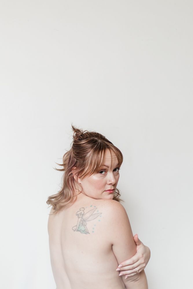 Artistic portrait showing a shoulder tattoo of a fairy against a minimalist white background.
