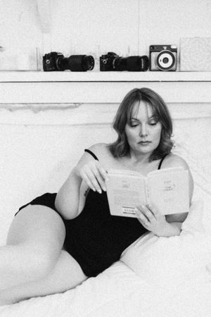 A black and white artistic photo series showing a figure in black lounging and reading while reclining on white bedding.