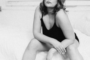 A black and white artistic portrait of someone in a dark sleeveless top sitting on a light colored surface.