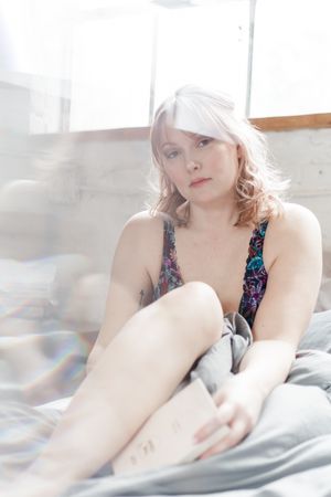 Person in floral print top reclining on white bedding in bright sunlit room.