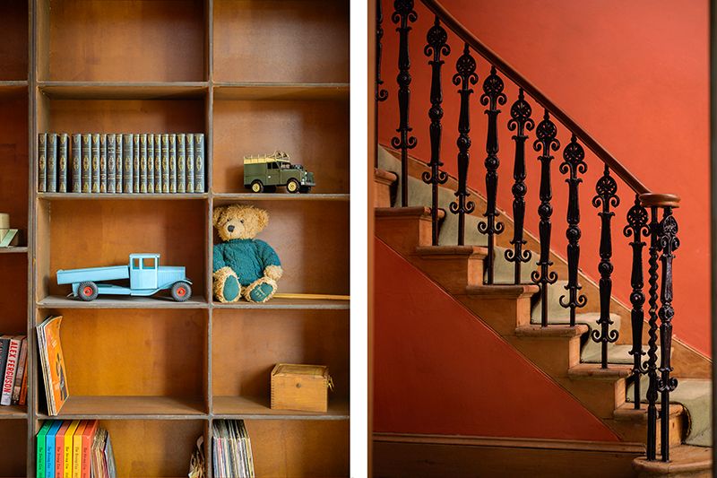 Wooden staircase with ornate black metal railing leads upward beside built-in shelving with orange-painted walls.
