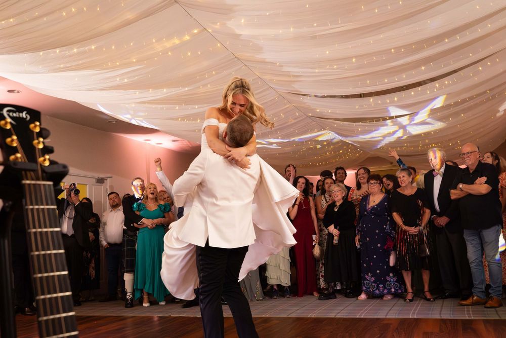 Wedding reception dance floor with guests celebrating under draped white fabric ceiling and warm lighting.