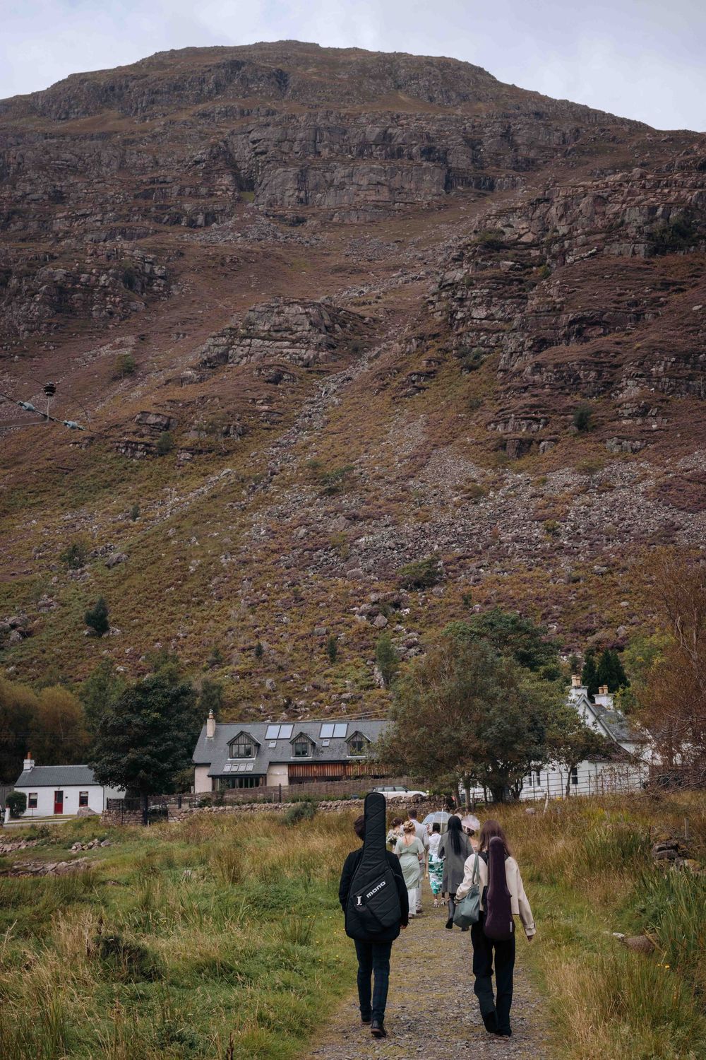 Scenic mountain landscape with small white houses nestled at the base of rugged brown cliffs in rural Scotland.