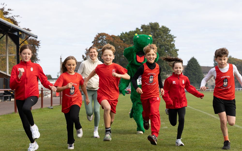 Children in red uniforms run and play together on a grassy field during an outdoor activity.