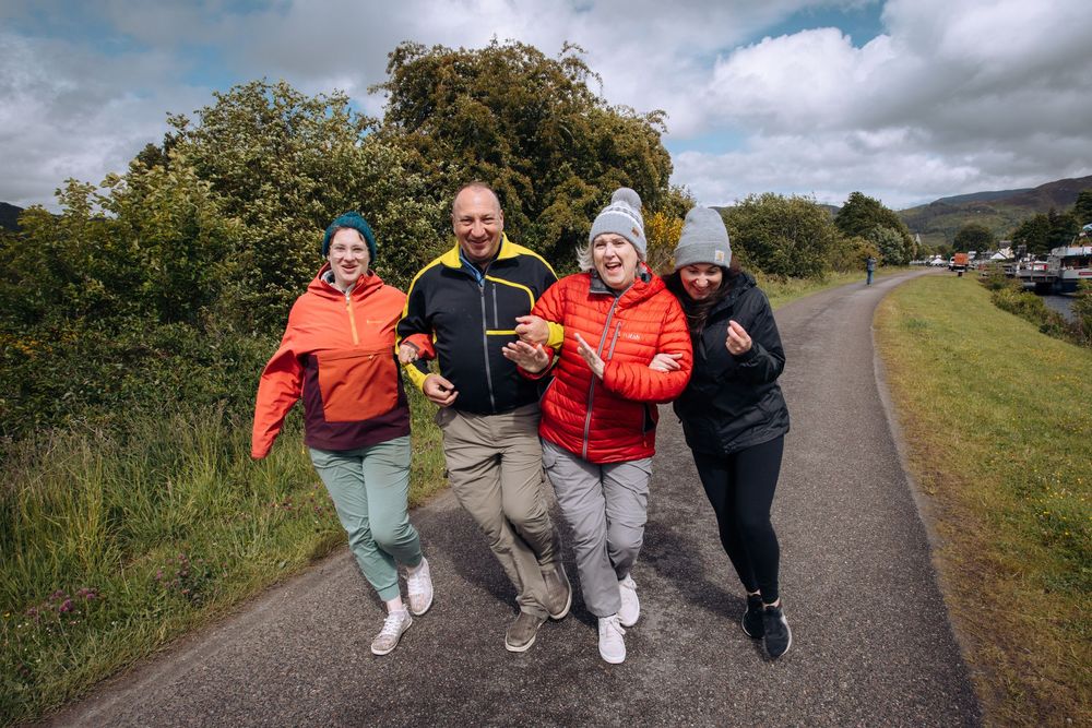 A group of people jumping and posing playfully on a path outdoors with cloudy skies overhead.