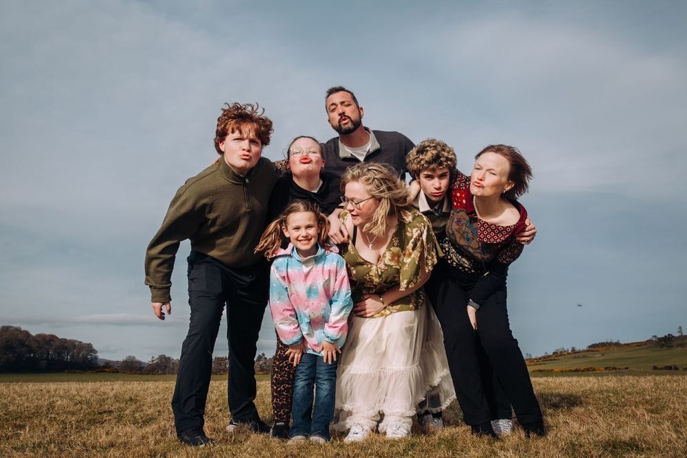 Family group poses together in casual attire against cloudy sky in outdoor field setting.