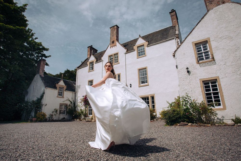 A flowing white dress twirls dramatically against the backdrop of a traditional white stone house.