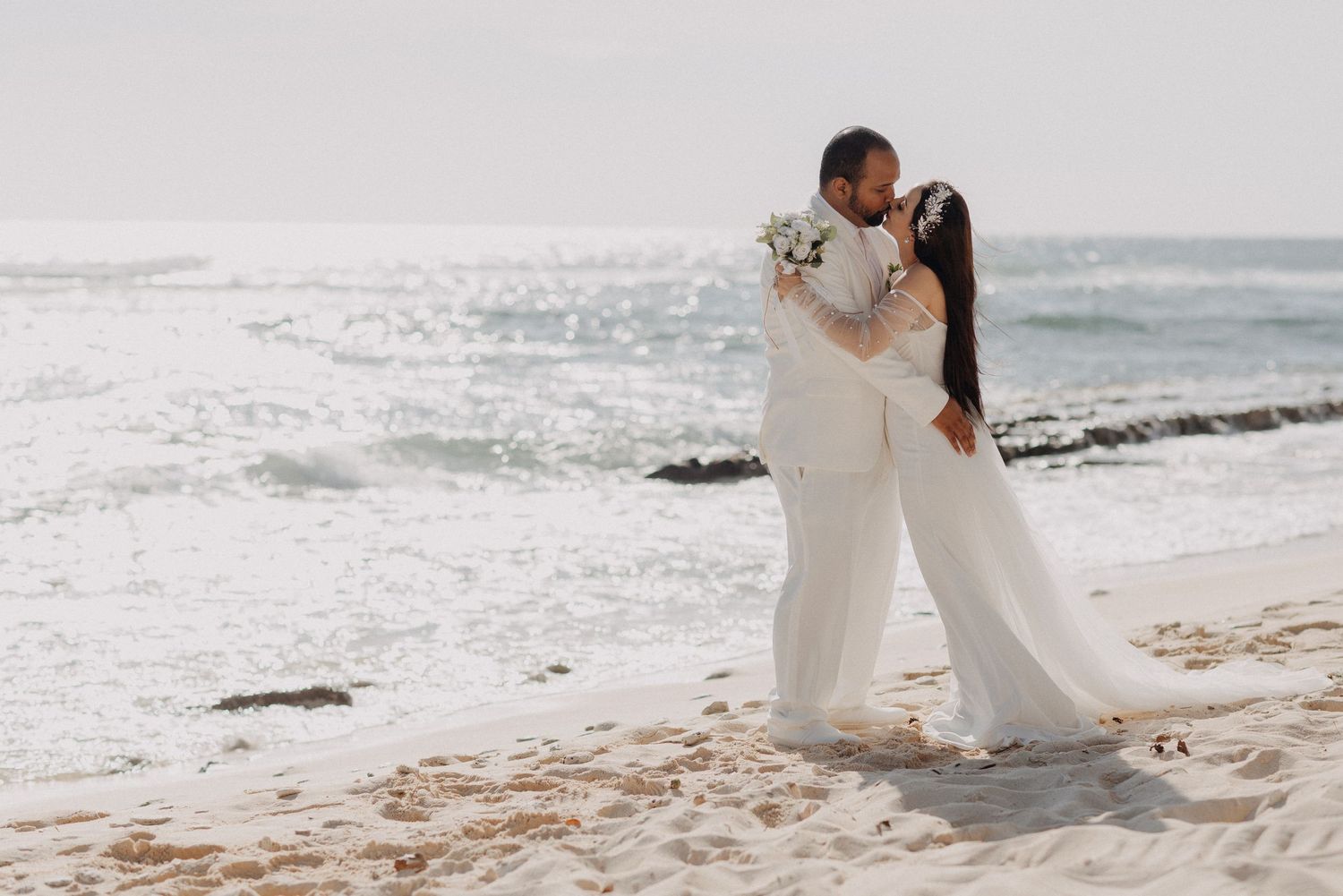 Romantic beach wedding photoshoot with waves crashing on sandy shore.