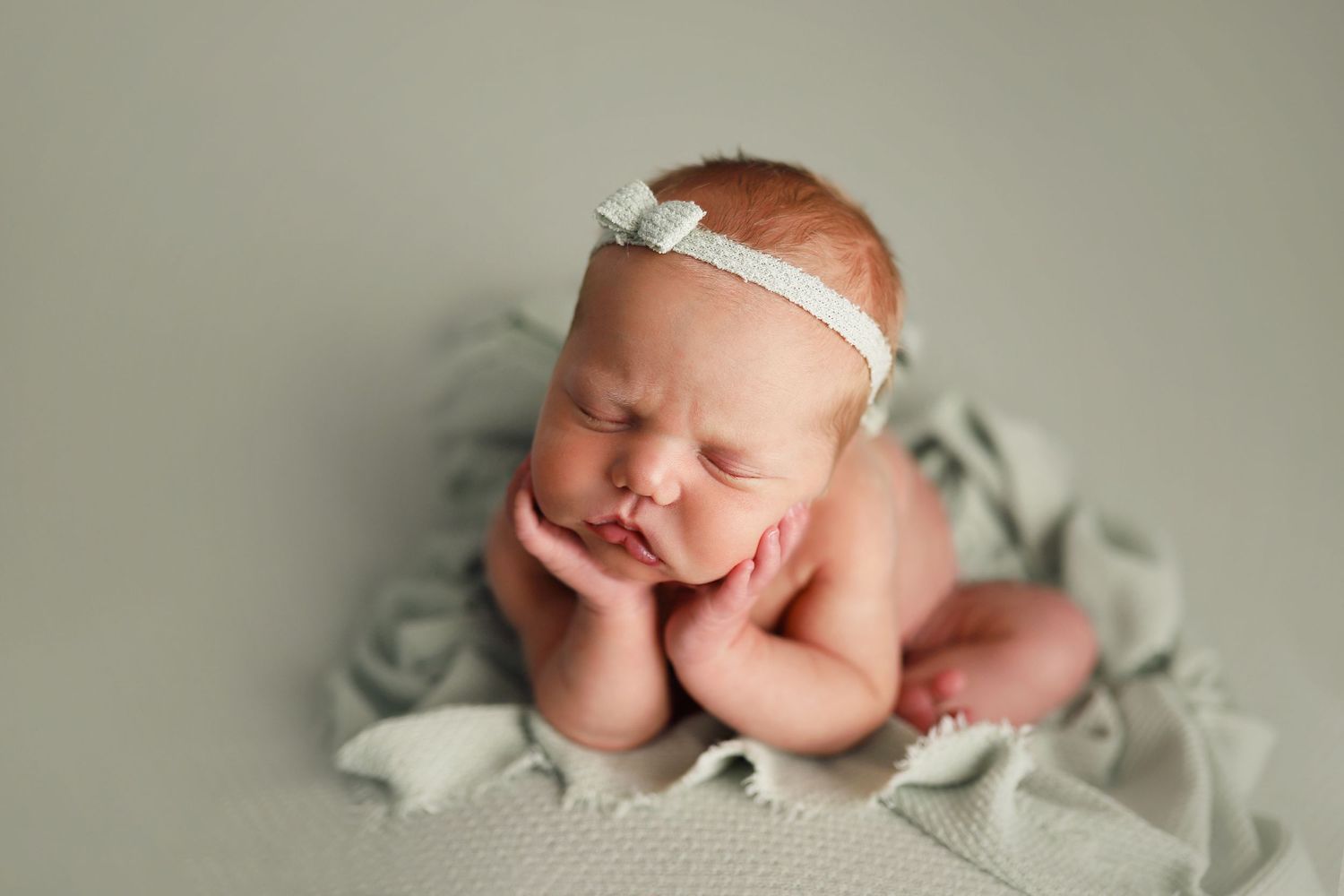 A series of seven connected photos showing a sleeping newborn baby in soft white fabric against a neutral background.