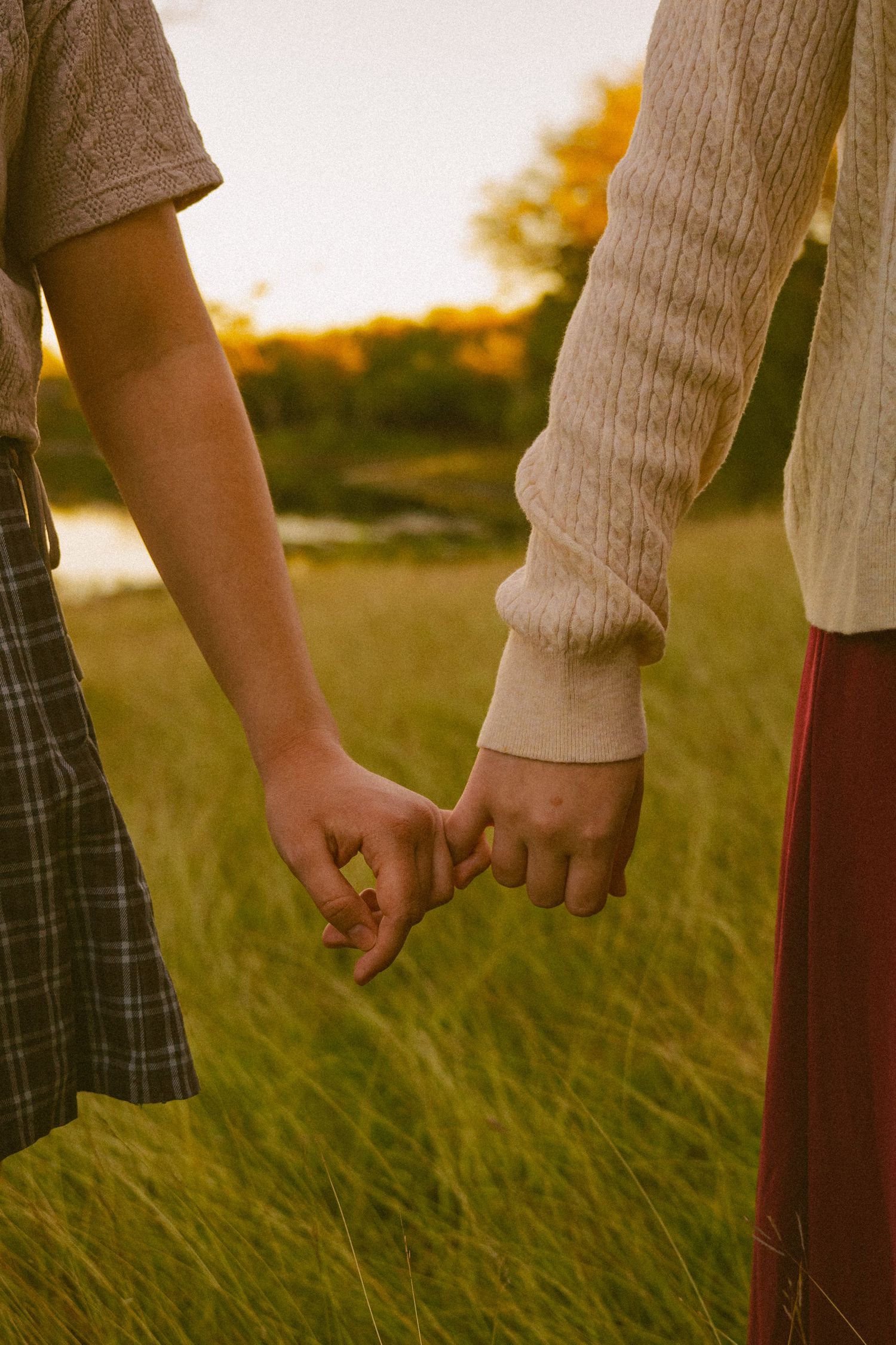 A couple sits together in a golden sunlit meadow during sunset, creating a romantic autumn atmosphere.
