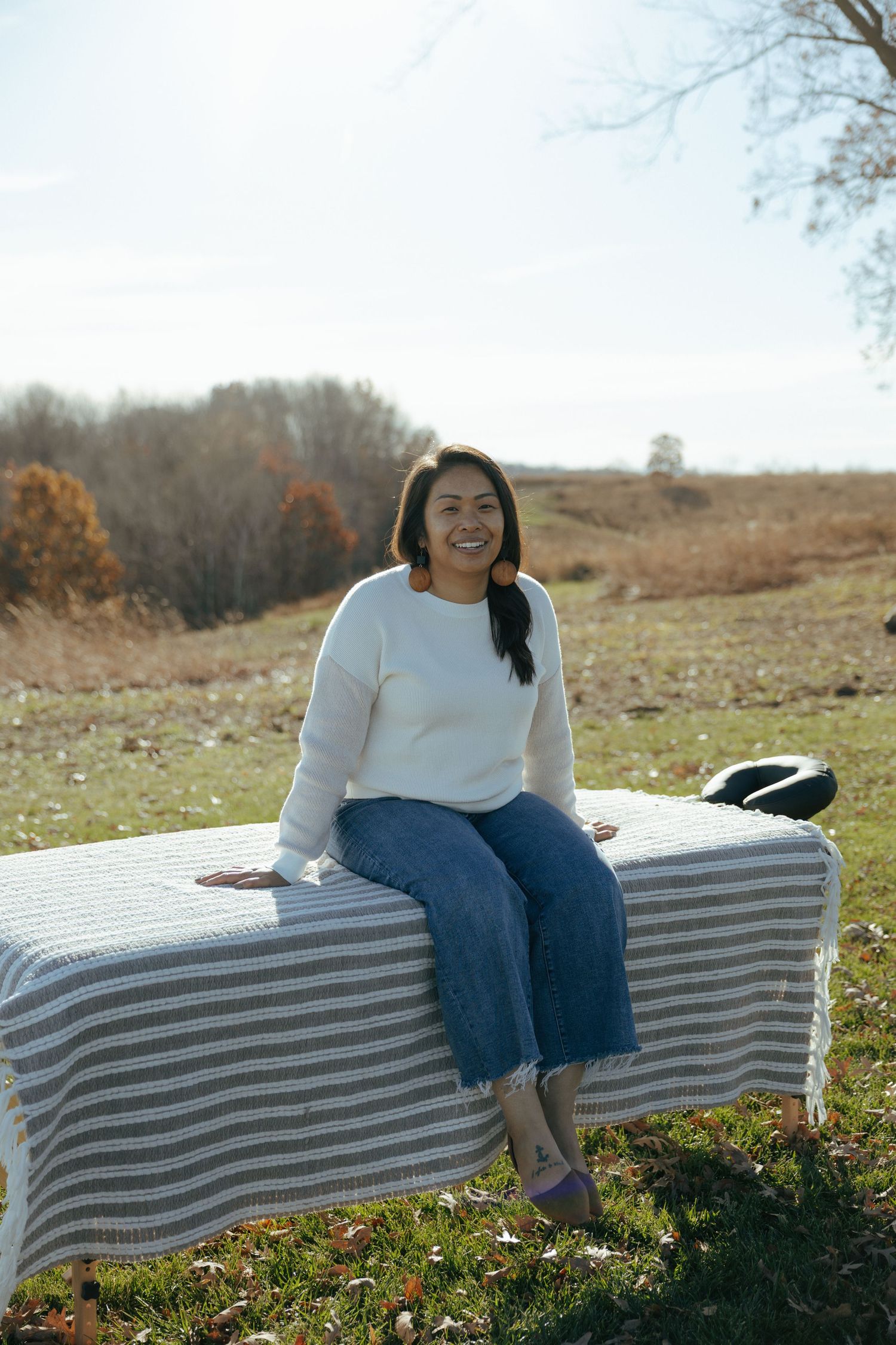 A person relaxes on a curved striped bench outdoors on a sunny autumn day with rolling hills in the background.