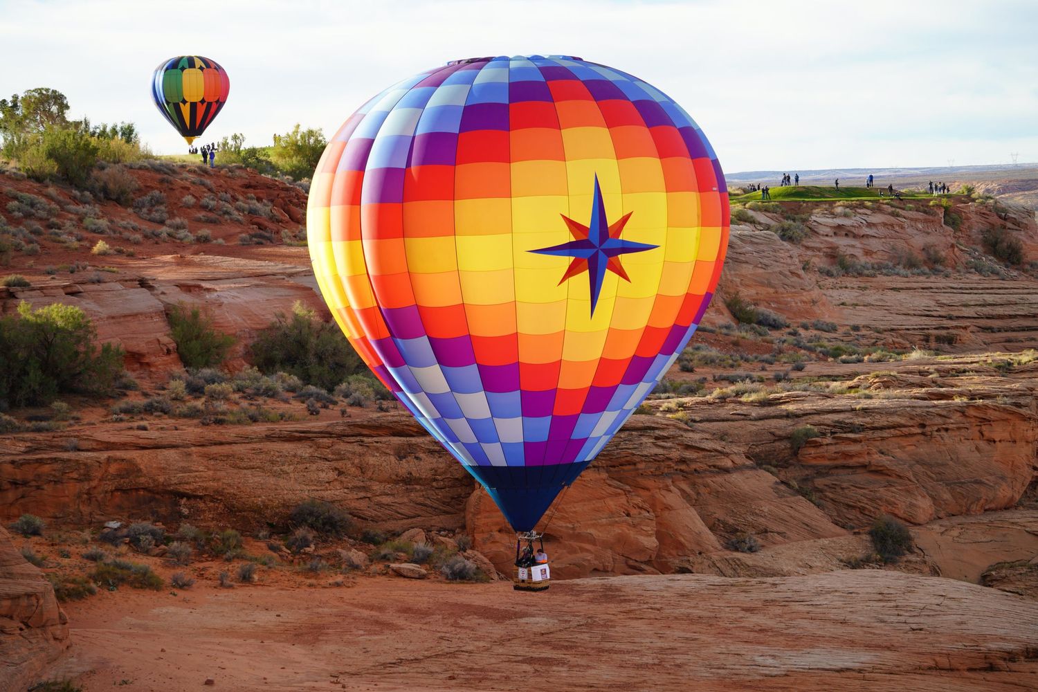 Colorful hot air balloons float above red rock formations in the desert landscape at sunrise.