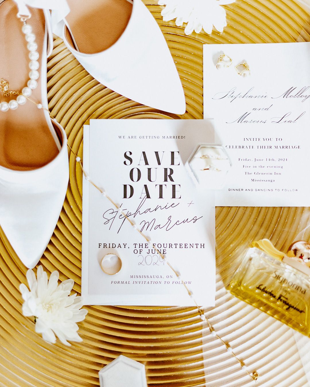 Wedding invitation suite with gold accents and white floral details on metallic textured background.
